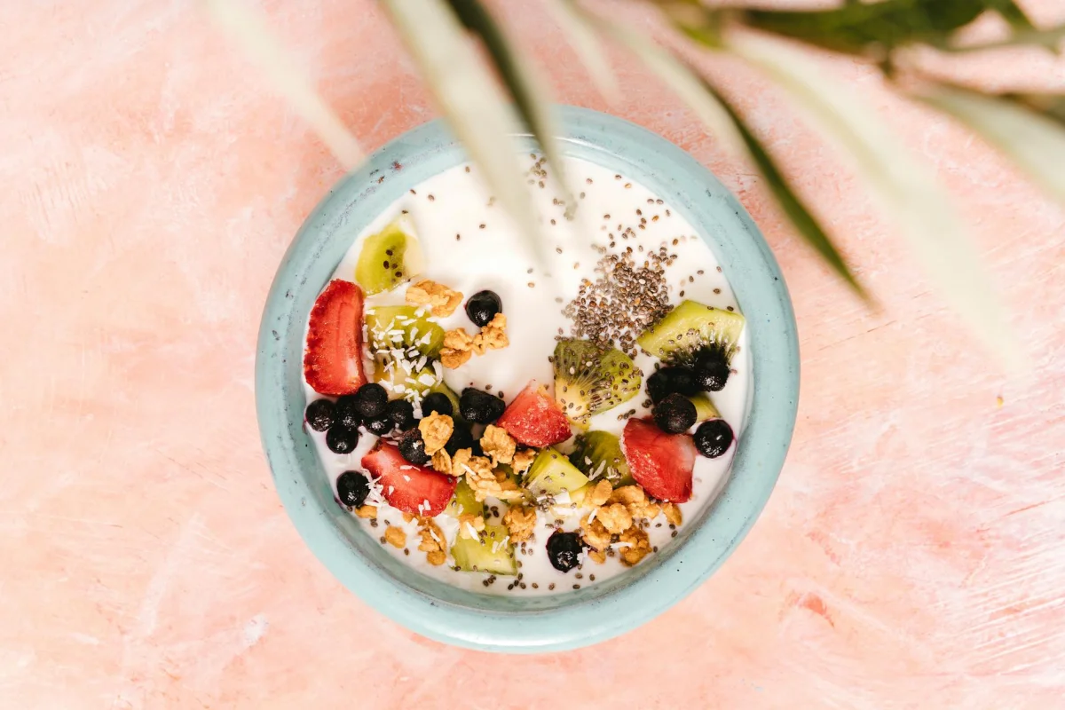 Bowl blanco con queso fresco batido, frutos rojos y semillas de chía sobre fondo de madera clara
