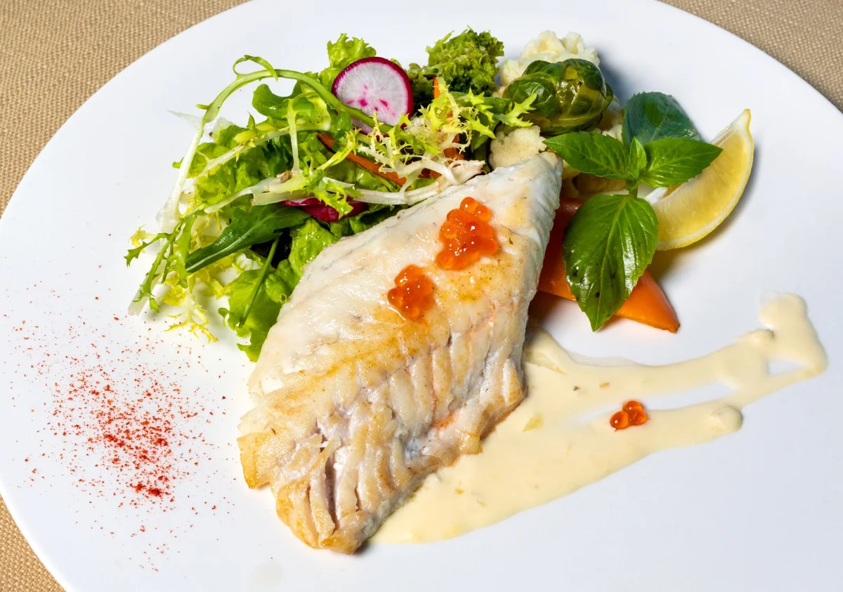 Filete de merluza blanca al vapor con rodajas de limón y perejil fresco en plato blanco