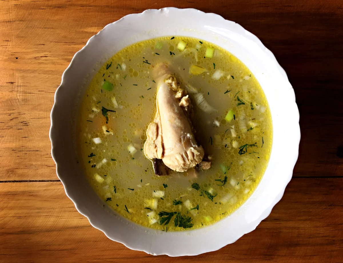 Bol de sopa de pollo casera con caldo dorado y trozos de pollo desmenuzado sobre una mesa de madera